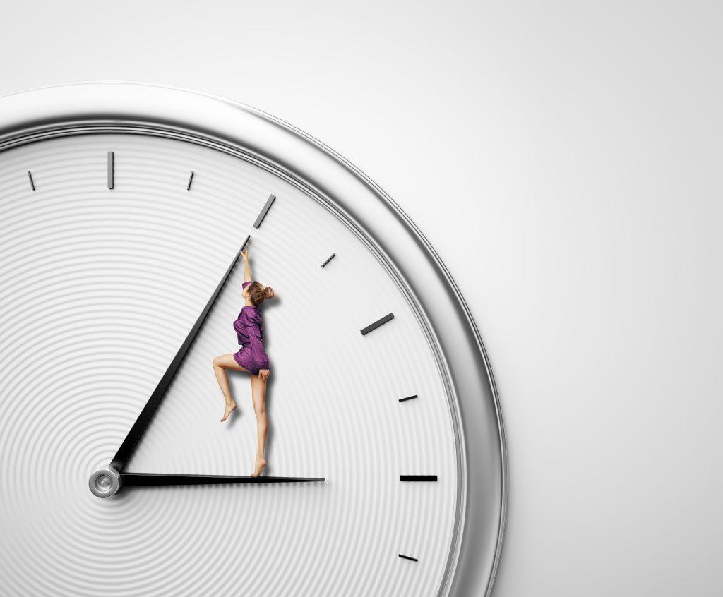 woman in a purple jumper standing on hour hand of clock and pushing minute hand backward